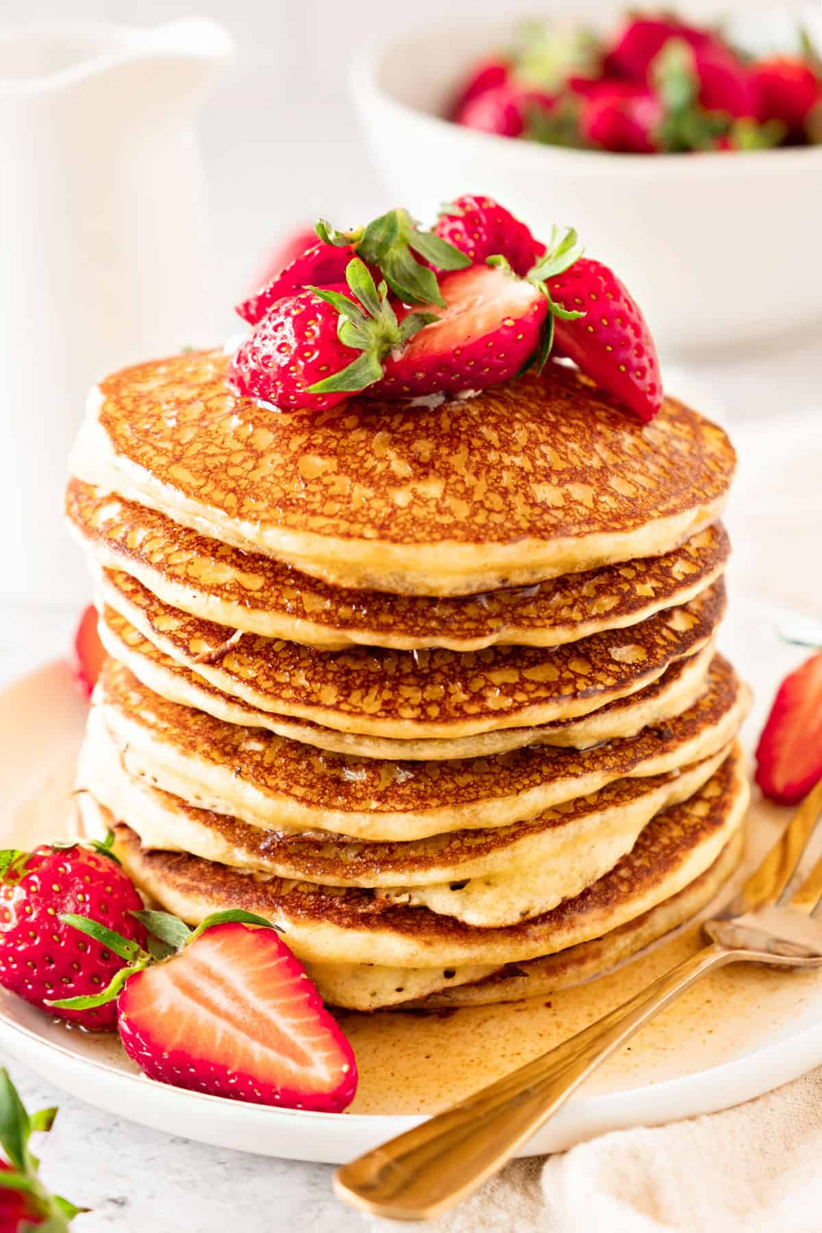 Tall stack of cottage pancakes with fresh strawberries and syrup. White plate and background. Silver fork.