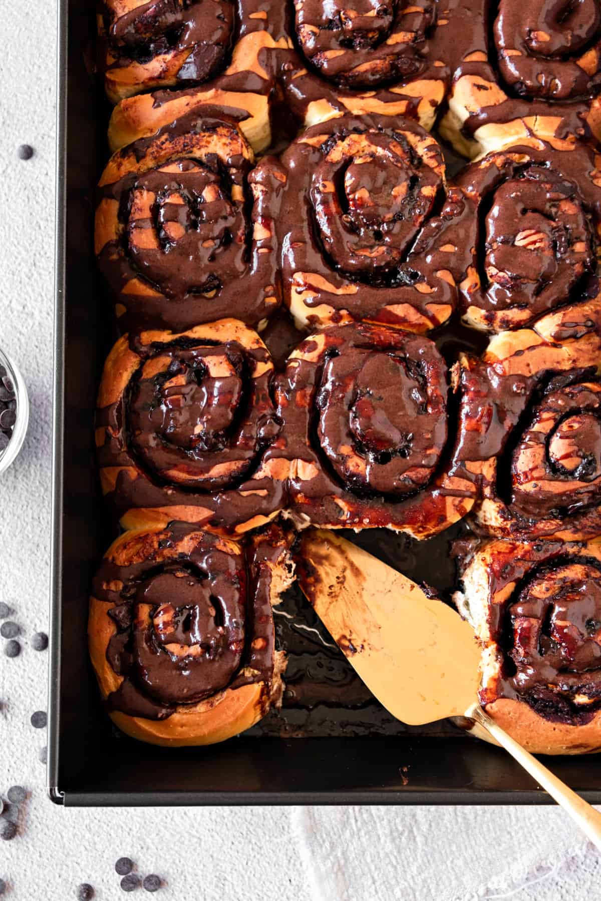 Cinnamon chocolate rolls with chocolate glaze on a dark pan. Golden server.