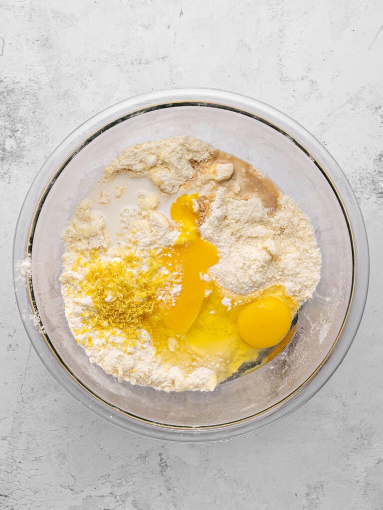 Eggs, lemon zest and flour mixture in a glass bowl. Light gray background, top view.