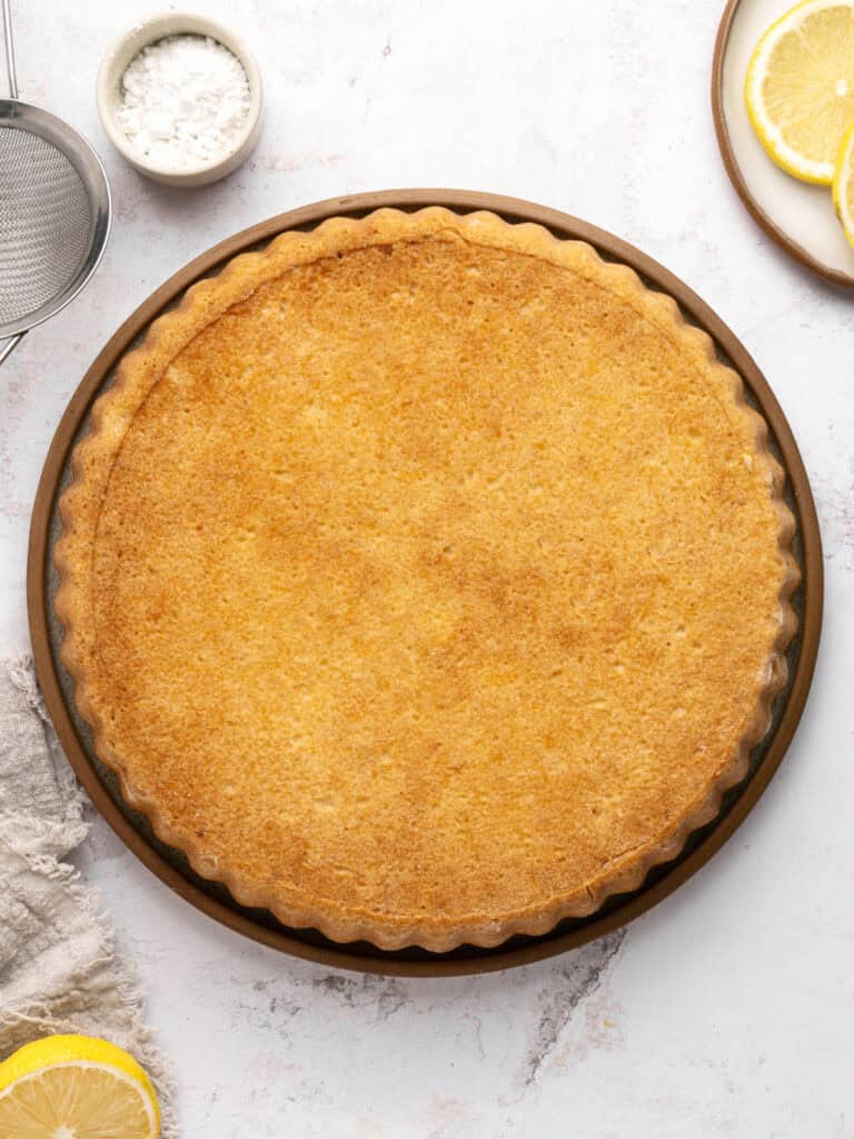 Baked double crust ricotta pie on a brown plate. Lemon slices, light gray surface, top view.