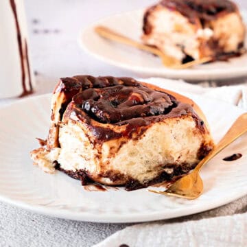White plates with glazed chocolate rolls. Gold forks, light gray background.