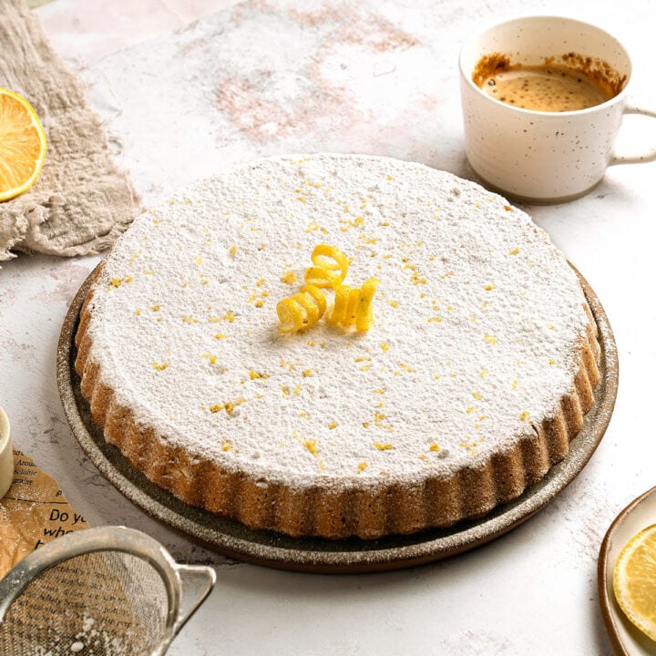 Whole double crust lemon ricotta pie with powdered sugar on a plate. White and beige background, coffee cup.