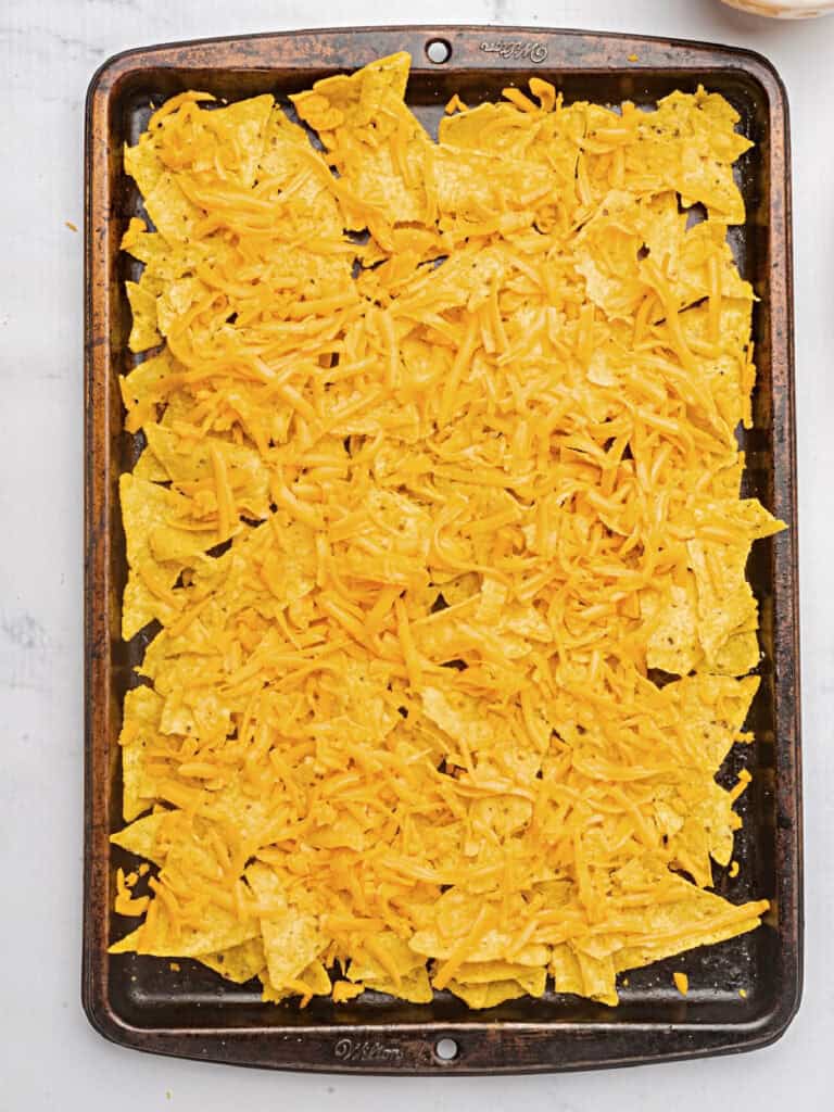 Metal tray with nachos and grated cheddar cheese. Top view.