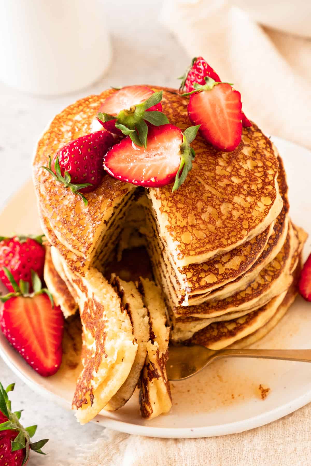 Strawberry and syrup topped stack of pancakes. Bite on a fork. White plate.