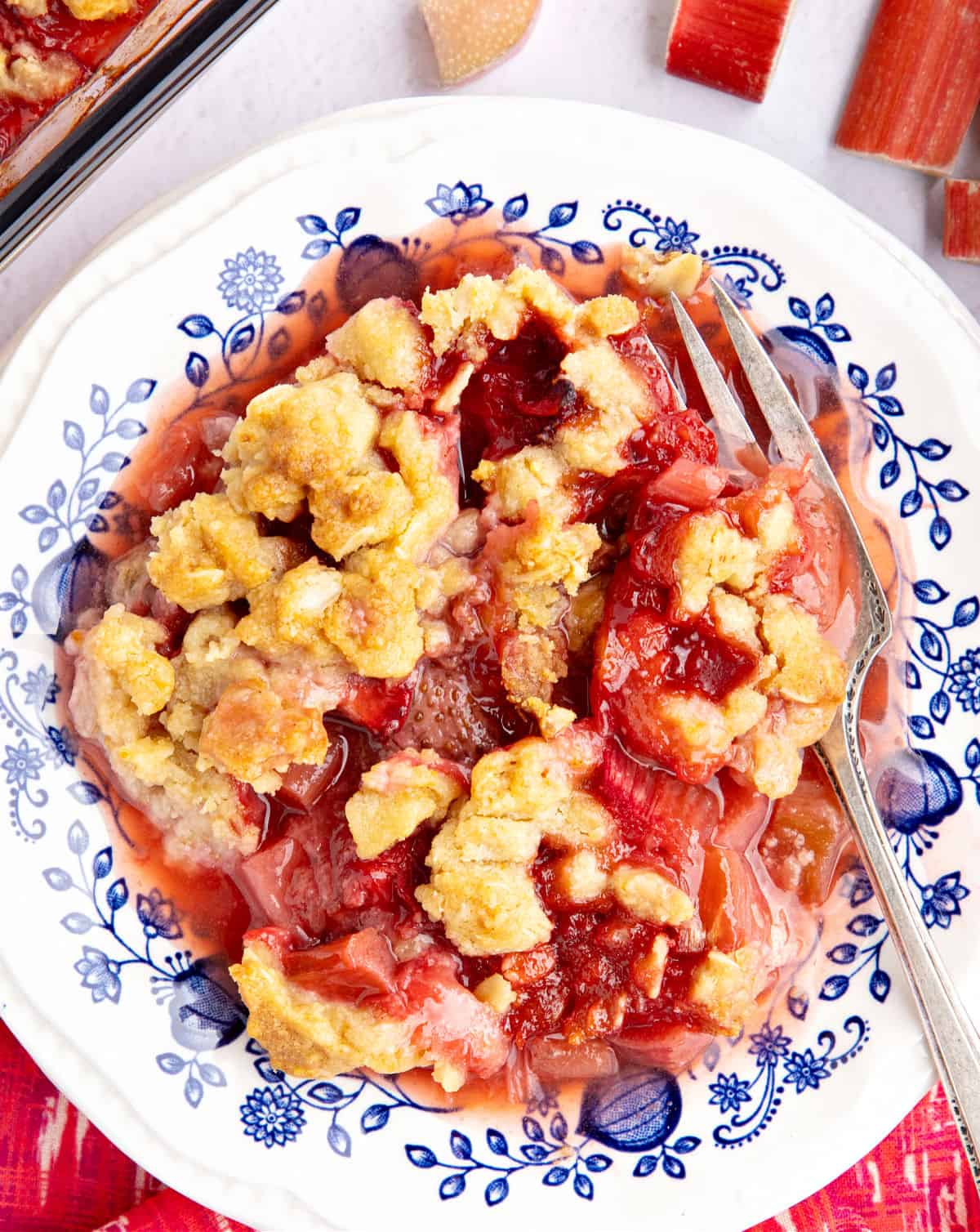 Blue and white plate with serving of rhubarb strawberry crisp. Silver fork.