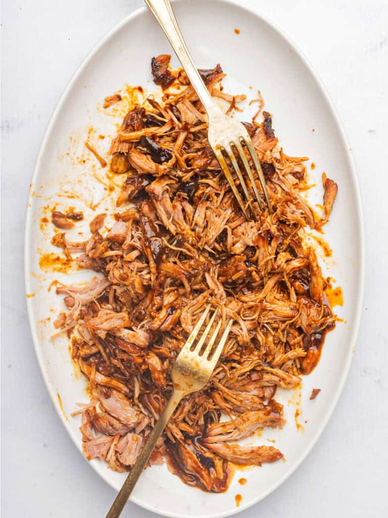 Two silver forks on a white platter with pulled pork. Top view.