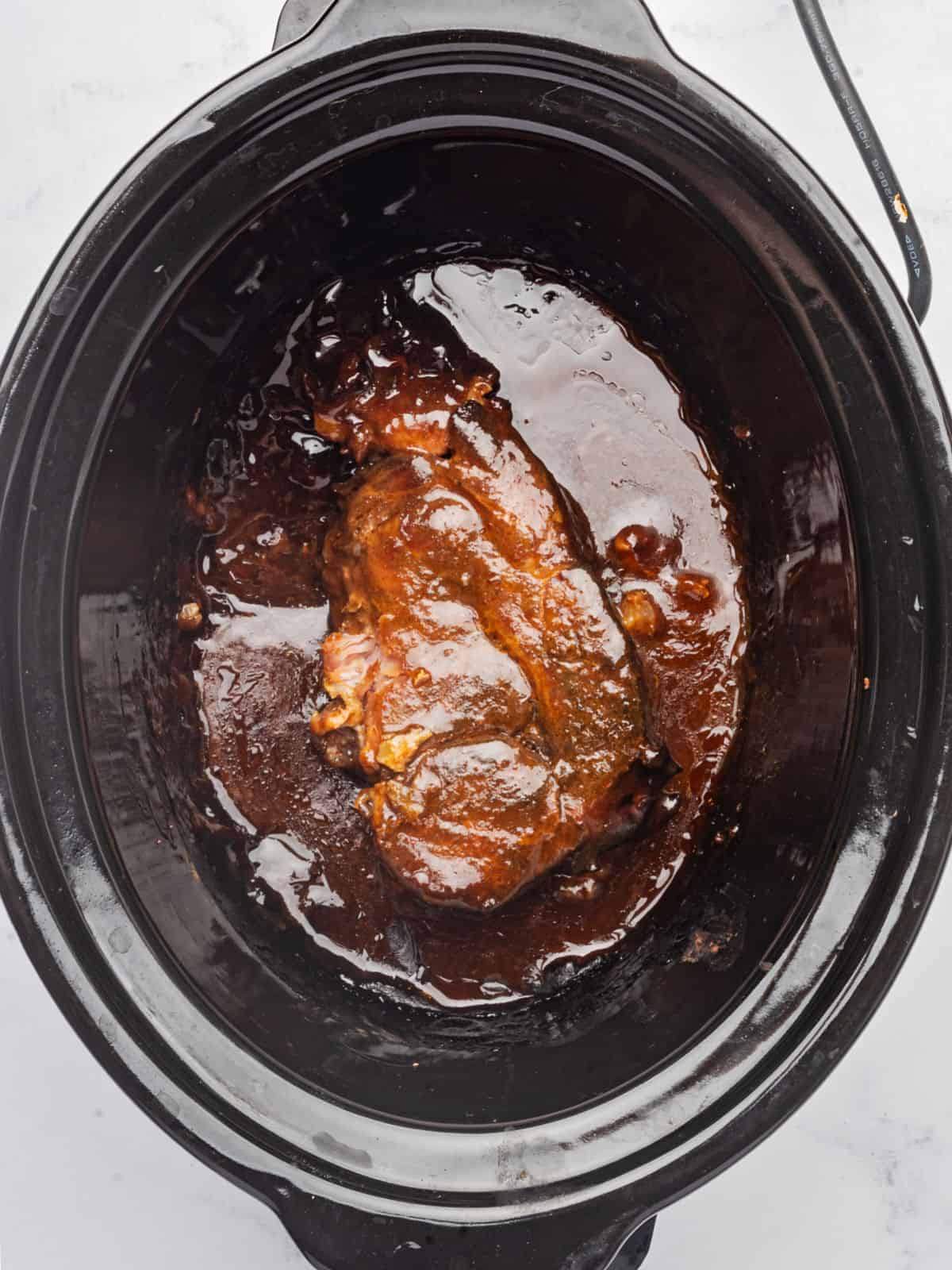 Slow cooker with cooked pork shoulder in barbecue sauce.