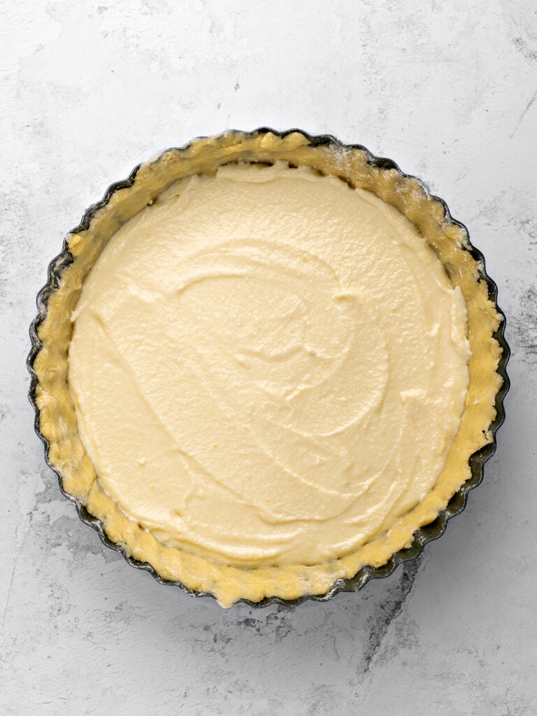 Unbaked pie crust in a dark pan with ricotta filling. Light gray background, top view.