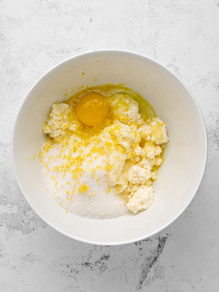 White bowl with ricotta, egg, sugar and lemon zest. Light gray surface, top view.