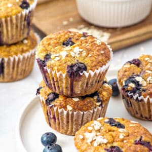 White plate with blueberry oat muffins in paper liners. White surface.