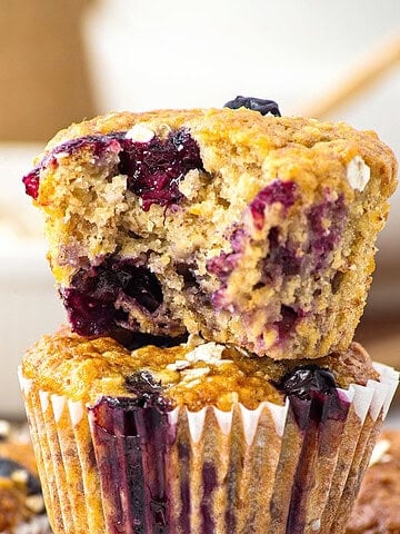 Two banana blueberry oat muffins in a stack, top one is bitten.