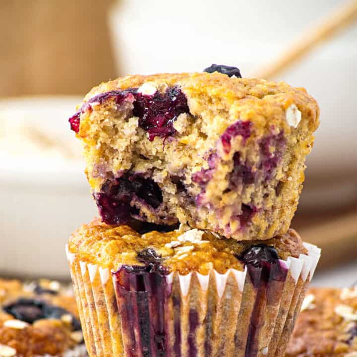Two banana blueberry oat muffins in a stack, top one is bitten.
