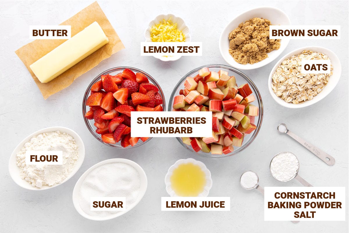 Bowls on a white surface with ingredients for strawberry rhubarb crips with oats.