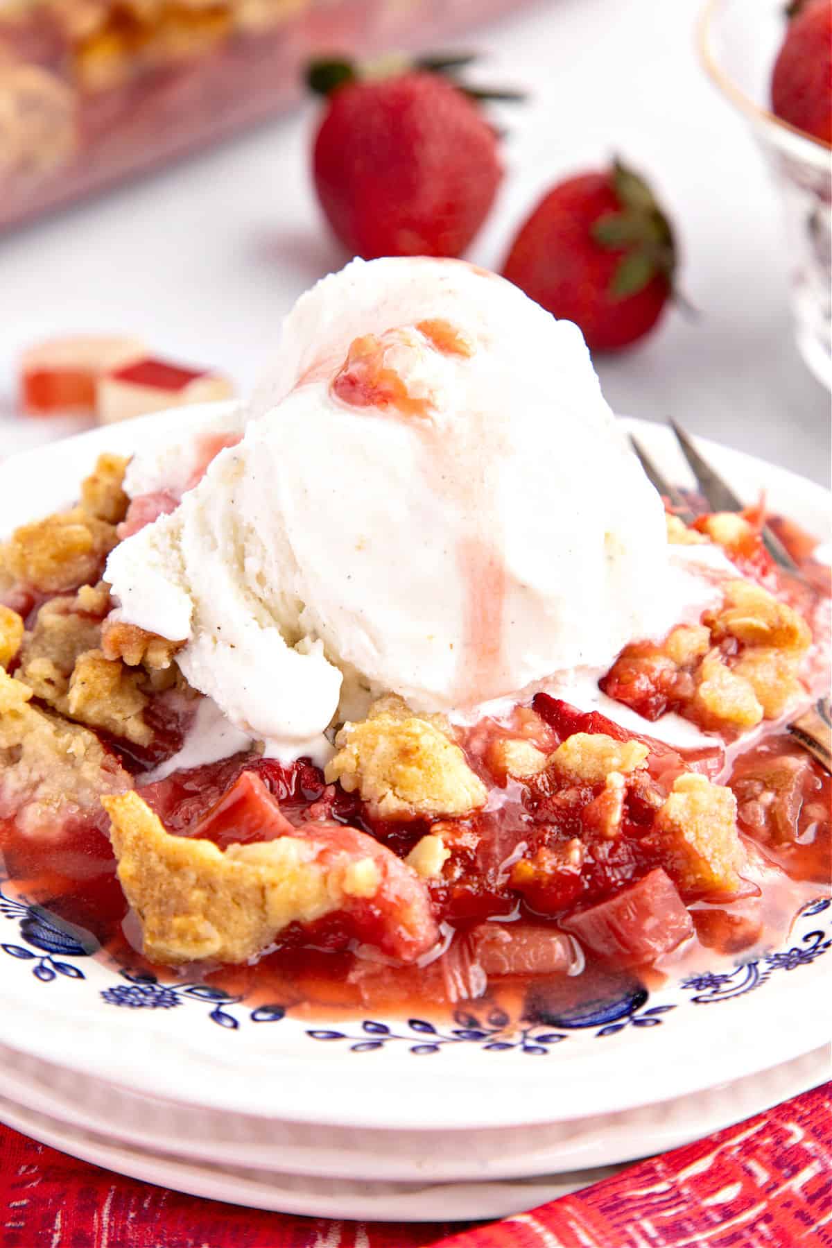 White blue plate with serving of strawberry rhubarb crisp with ice cream.