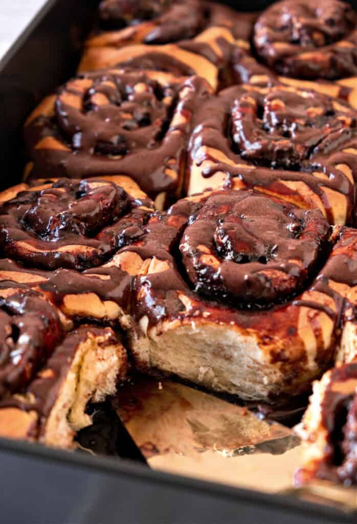 Black metal baking tray with chocolate glazed rolls.
