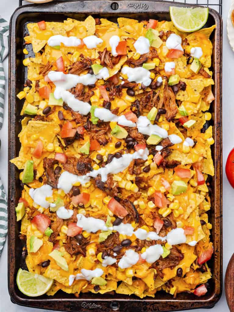 Sauce drizzled over pork loaded nachos on a metal tray.