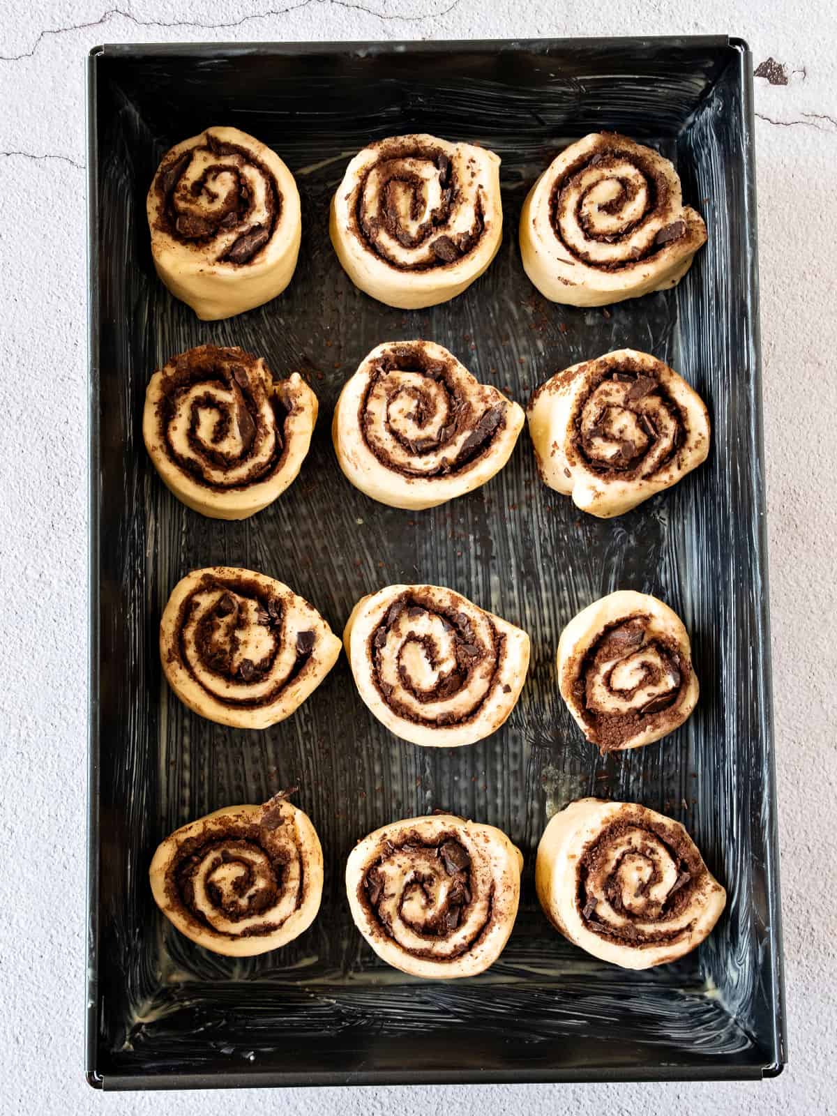 Dark metal pan with chocolate rolls before rising. Top view.