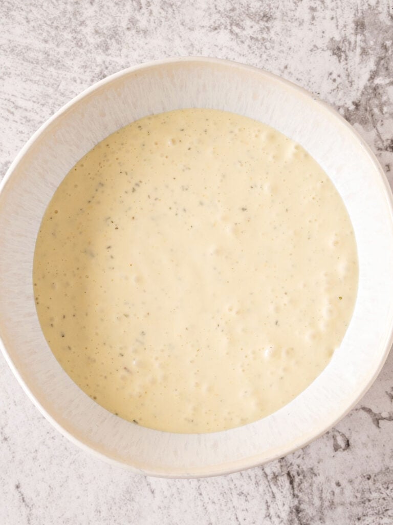 White bowl with mayo yogurt salad dressing. Gray background.