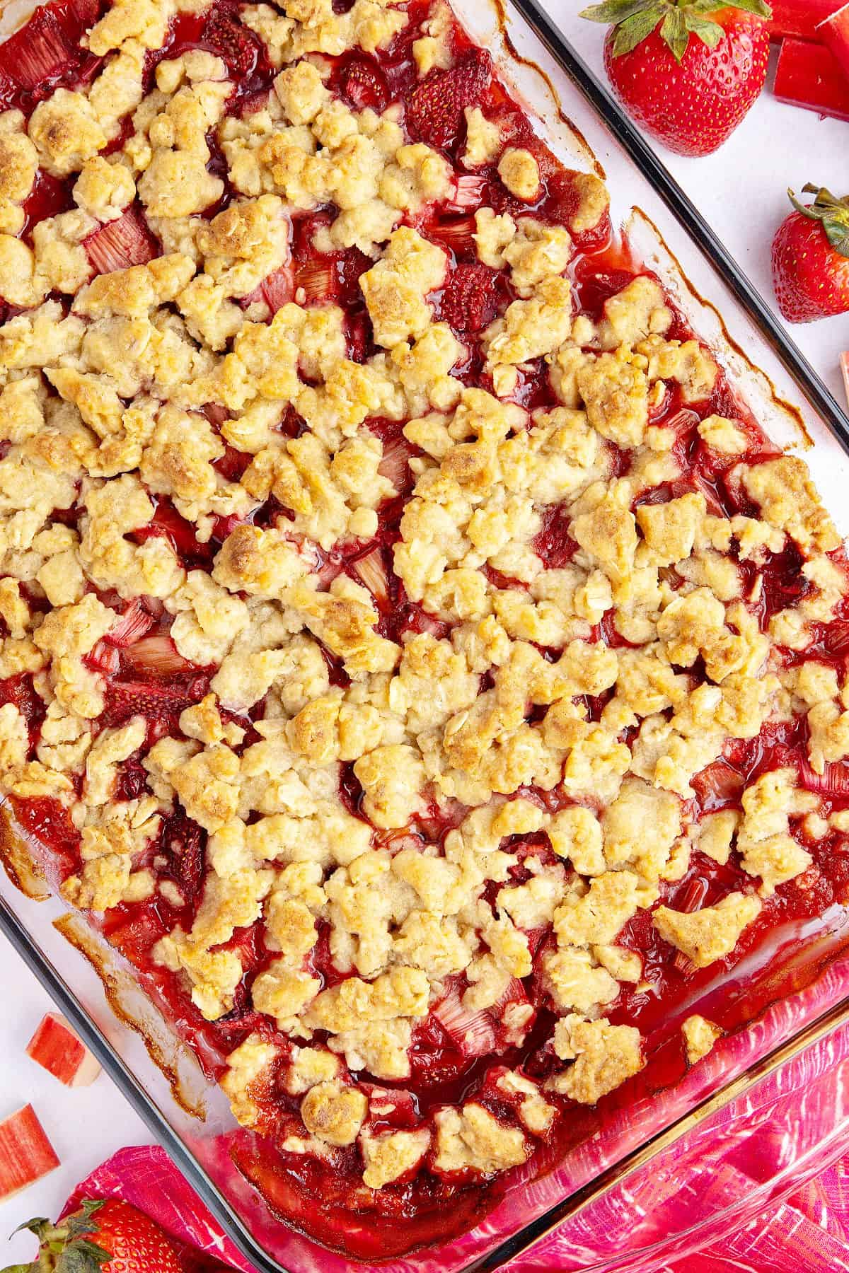 Glass baking dish with strawberry rhubarb crisp. Berries, red cloth.