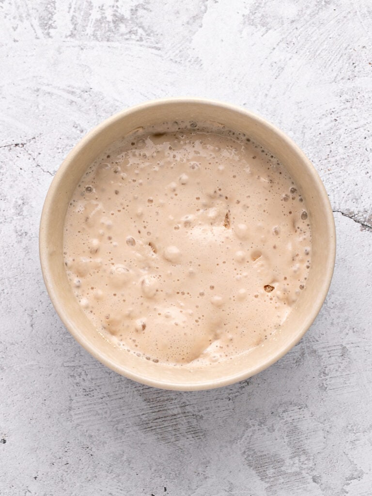 Beige bowl with bubbly yeast and liquid. Light gray background.