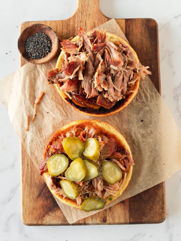Assembling pulled pork burgers with pickles on a wooden board. 
