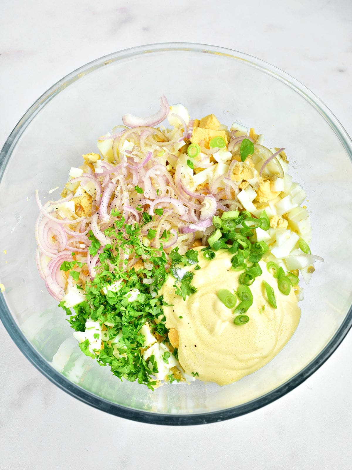 Glass bowl with ingredients for egg salad. Light gray background.