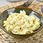 Mayo egg salad in a dark brownish green bowl. Raffia plate placer.