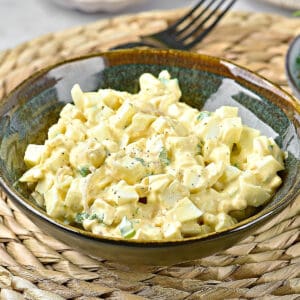 Mayo egg salad in a dark brownish green bowl. Raffia plate placer.