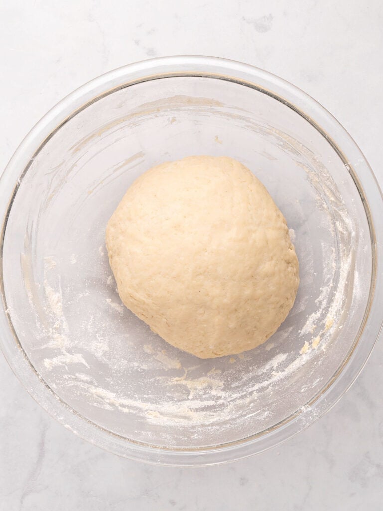 Ball of dough in a glass bowl. Light gray background.