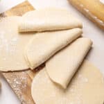 Several empanada dough discs on a wooden board.