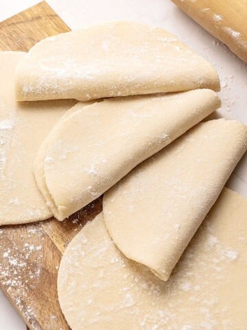 Several empanada dough discs on a wooden board.