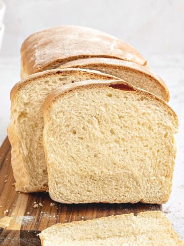 Sliced white sandwich bread on a wooden board. Light gray background.
