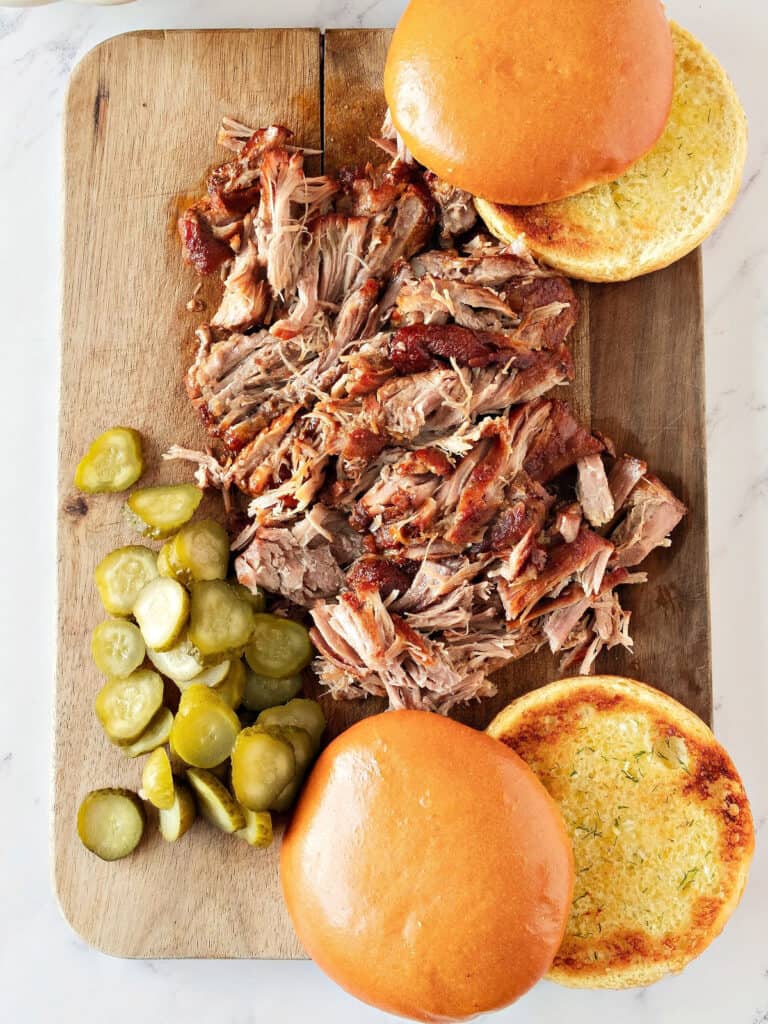 Wooden board with pulled pork, pickles and burger buns. White background.