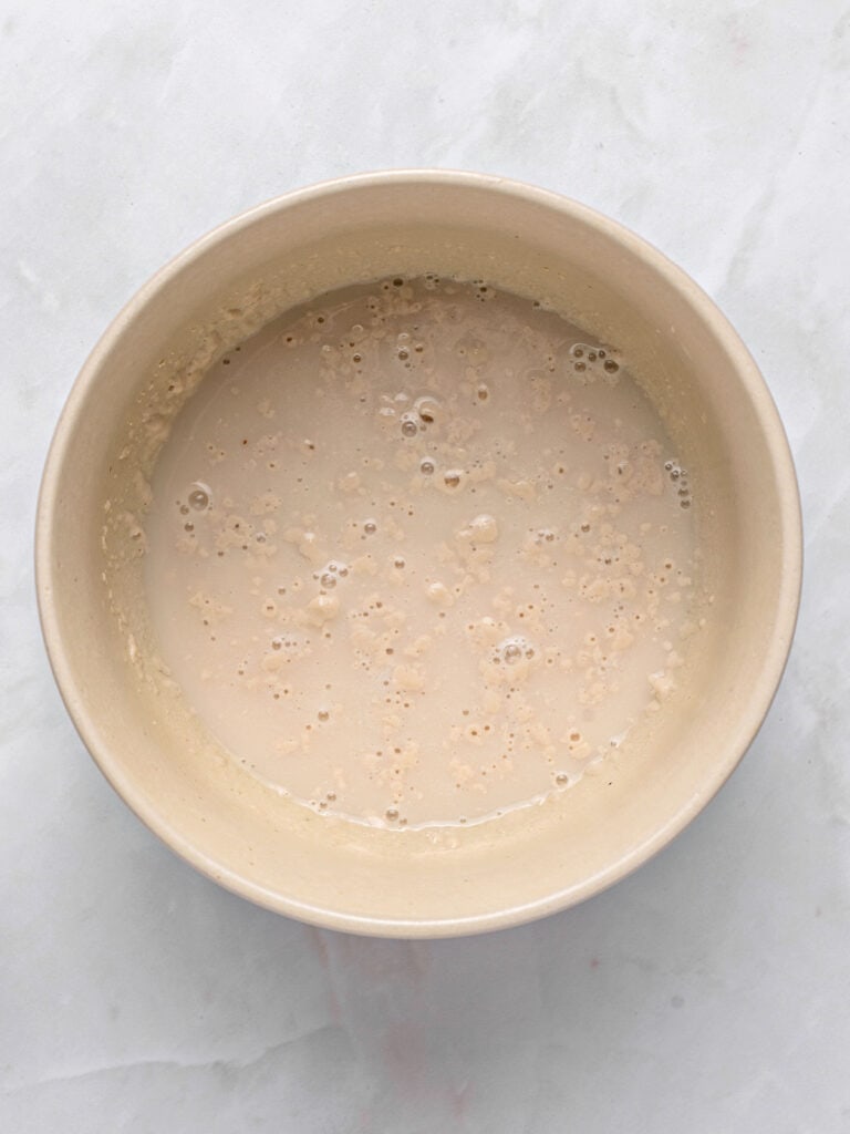 Beige bowl with yeast and liquid. Light gray background.