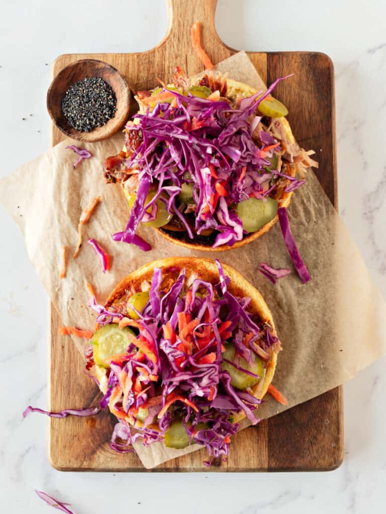 Coleslaw topped pork burger buns before closing. Wooden board.