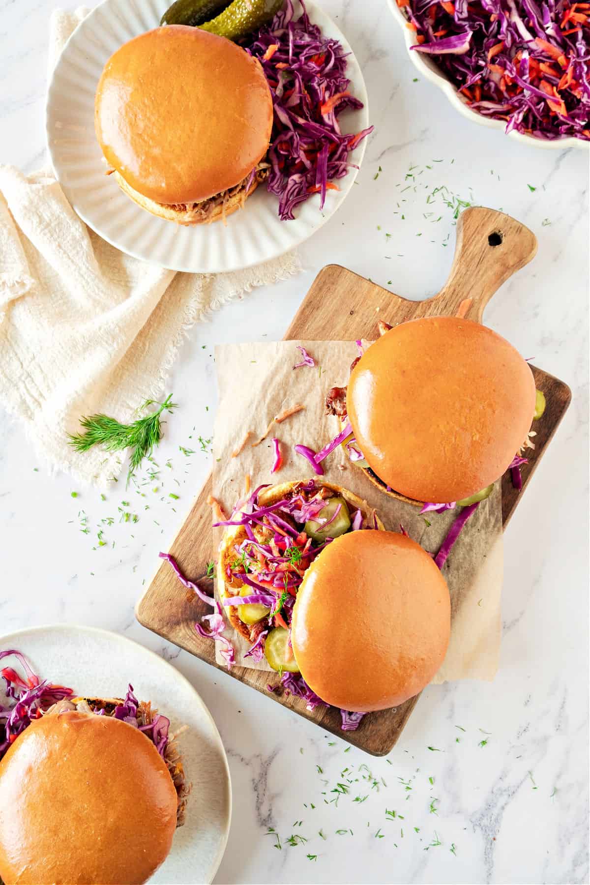Top view of several pork burgers with coleslaw. Wooden board, white plates, marbled surface.