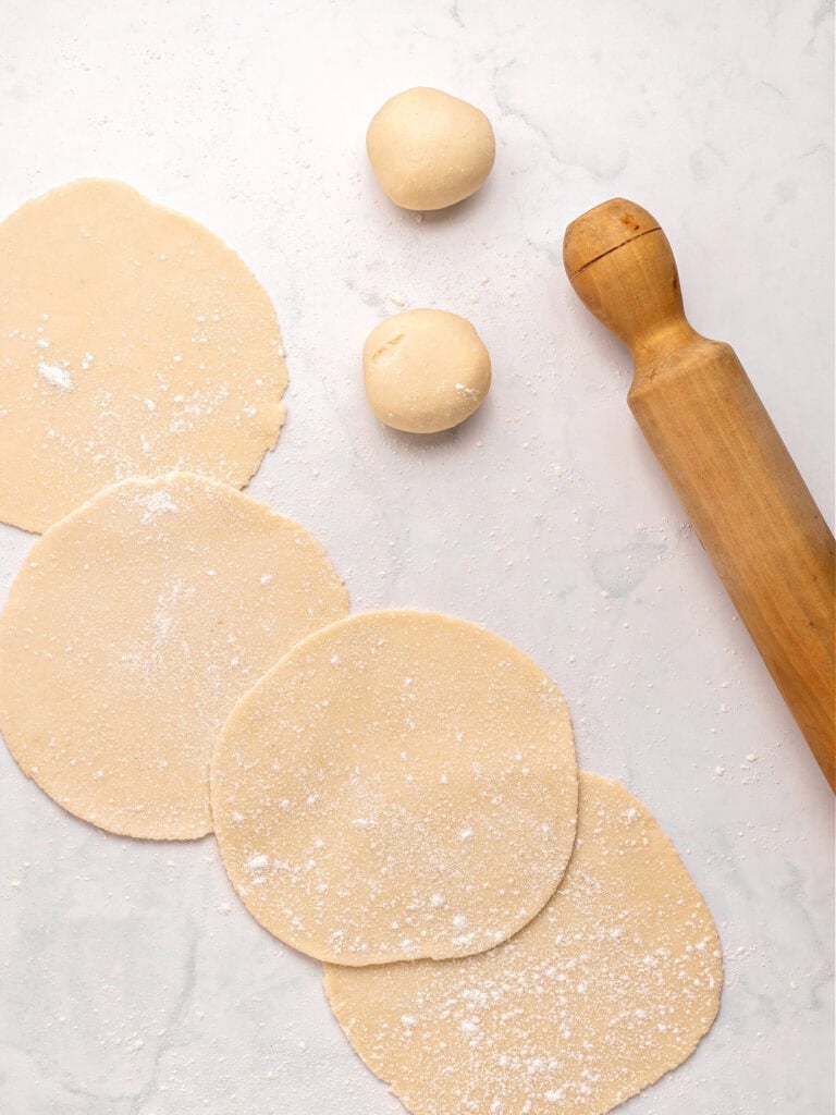 Rolling pin, empanada discs and dough balls on a light gray surface.