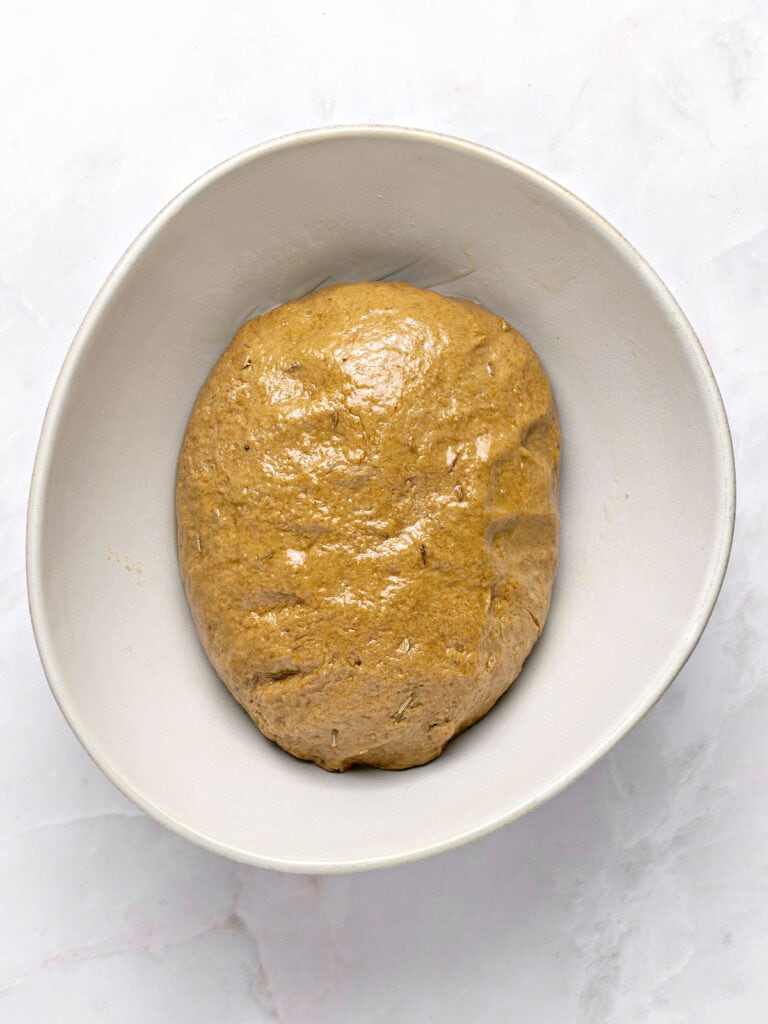 Whitish bowl with rype bread dough. Light gray background.