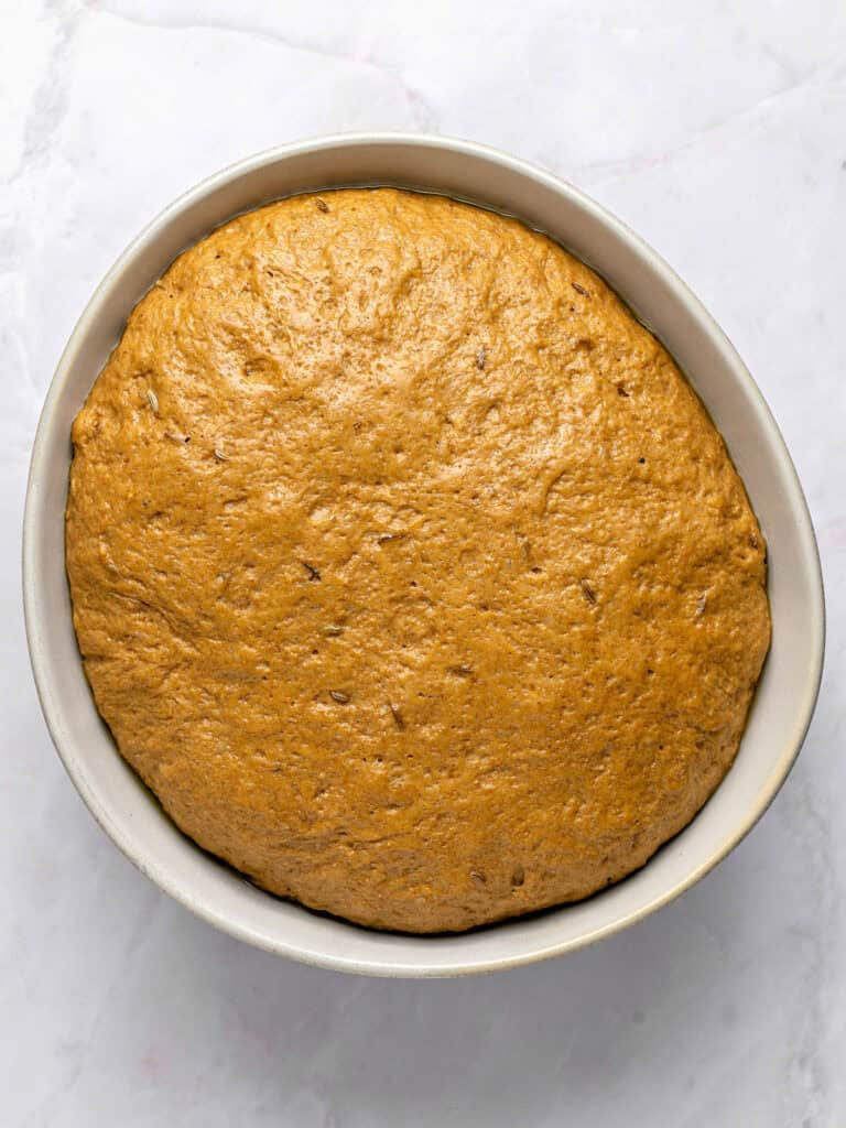 Proofed rye bread dough in a light gray bowl and surface.