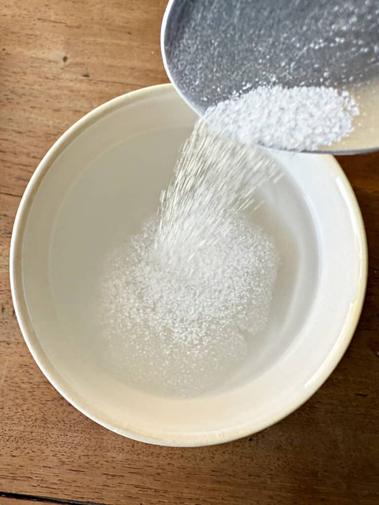 Adding salt to white bowl of water. Wood surface.