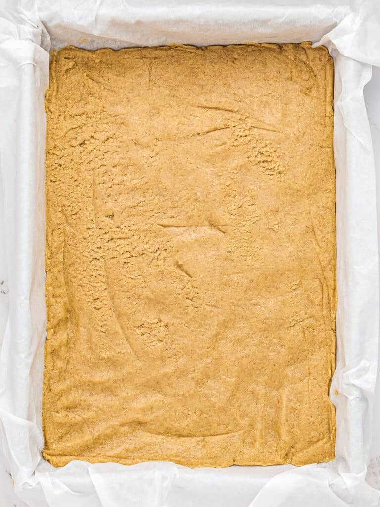 Shortbread graham cracker base in a parchment lined baking pan.