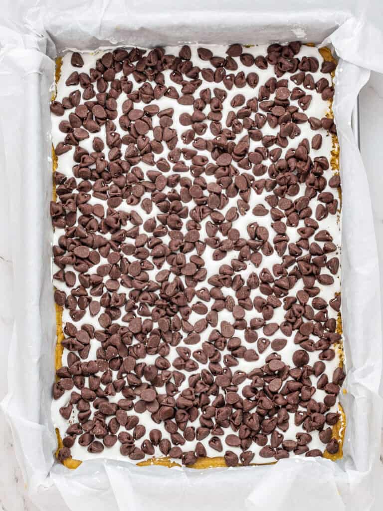 Marshmallow and chocolate chip layer of s'mores bars in a parchment-lined pan.