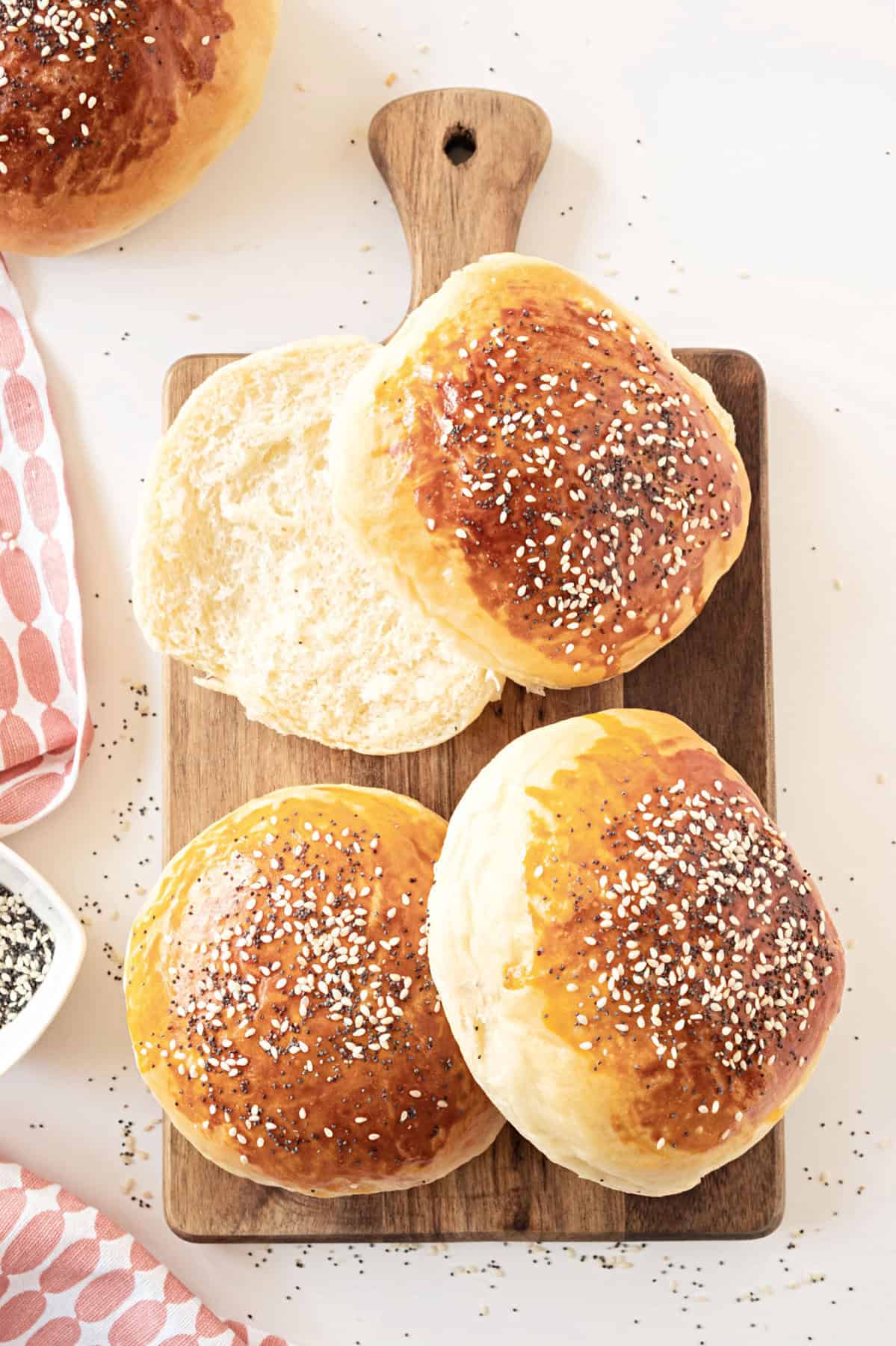 Wooden board with hamburger buns with seeds. White surface. 