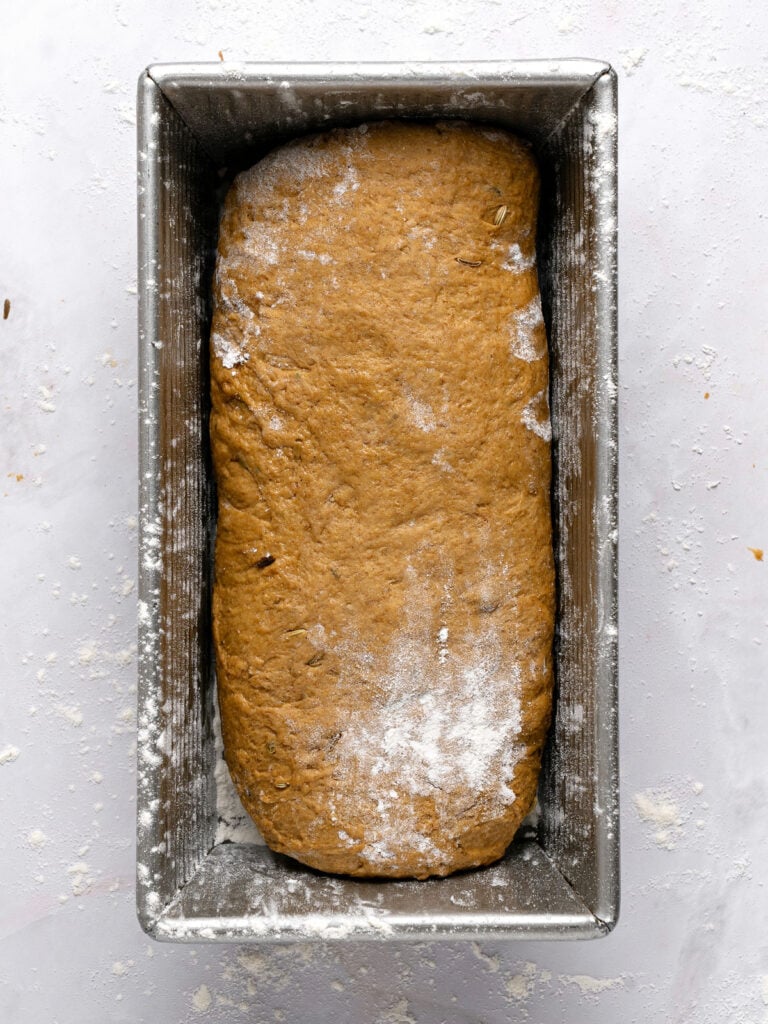 Metal loaf pan with rye bread before rising. Light gray background.