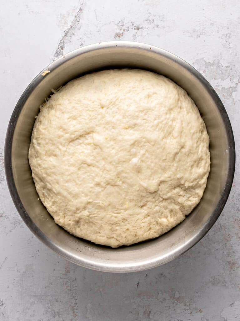 Risen white bread dough in a metal bowl. Light gray background.