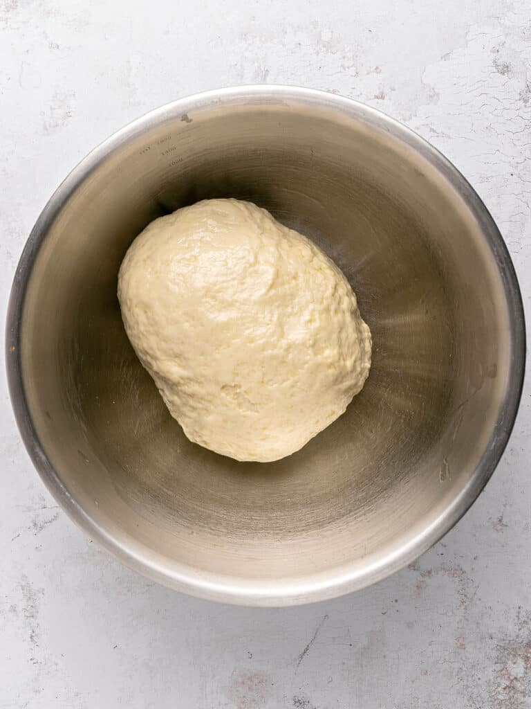 Metal bowl with white bread dough. Light gray background.