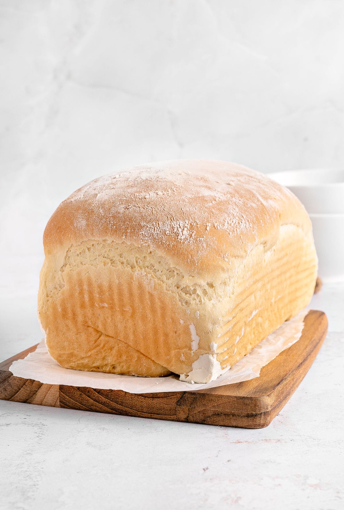 Loaf of white sandwich bread on a wooden board. Light gray background.