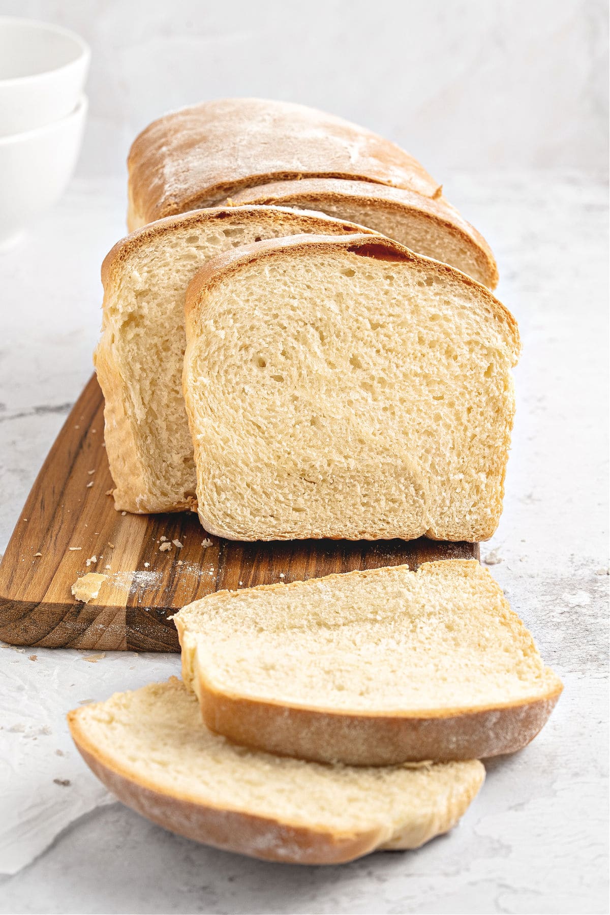 White sandwich bread, sliced, on a wooden board. Light gray background.