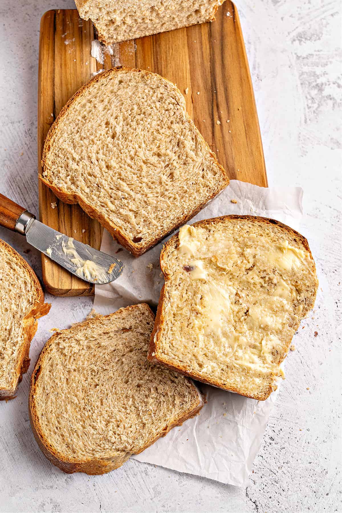 Several slices of whole wheat sandwich bread on a wooden board and white background.