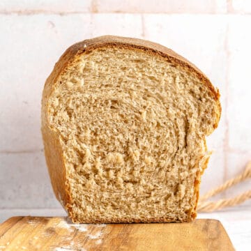 Halved whole wheat bread loaf on a wooden board. Tile background.